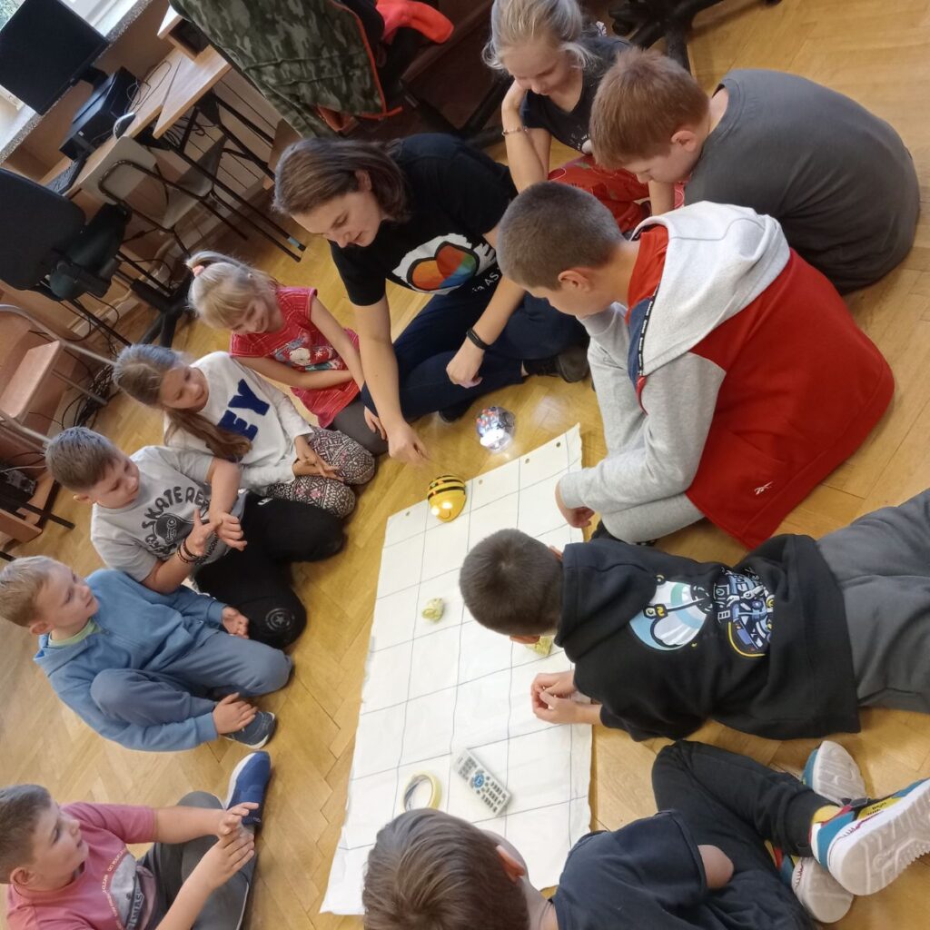 Grupa dzieci steruje robotem Bee-Bot na planszy podczas zajęć edukacyjnych