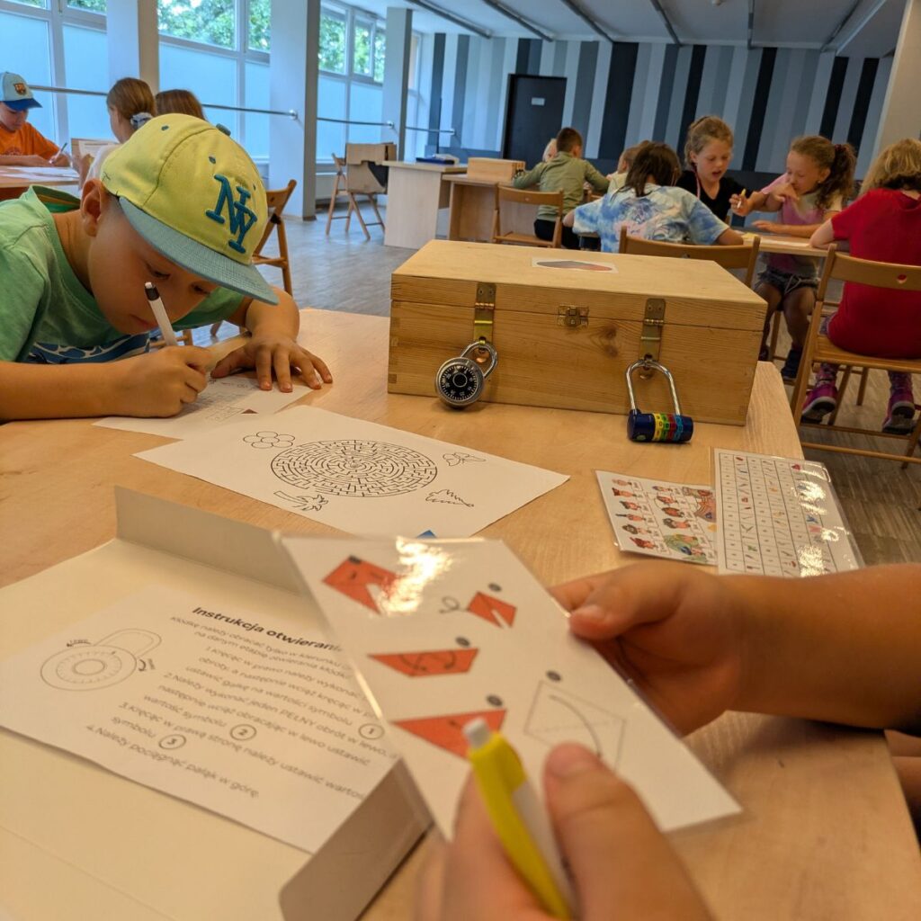 Dzieci rozwiązują zadania logiczne przy stole podczas geometrycznego escape roomu