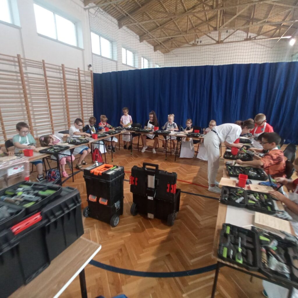Dzieci pracują przy stołach z narzędziami podczas zajęć technicznych w sali gimnastycznej