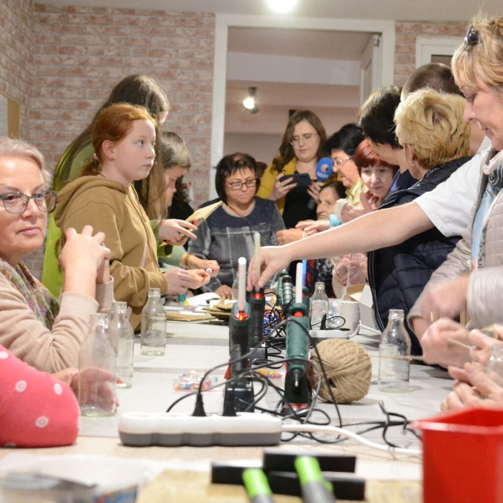 Uczestnicy warsztatów rękodzielniczych pracują przy wspólnym stole z narzędziami