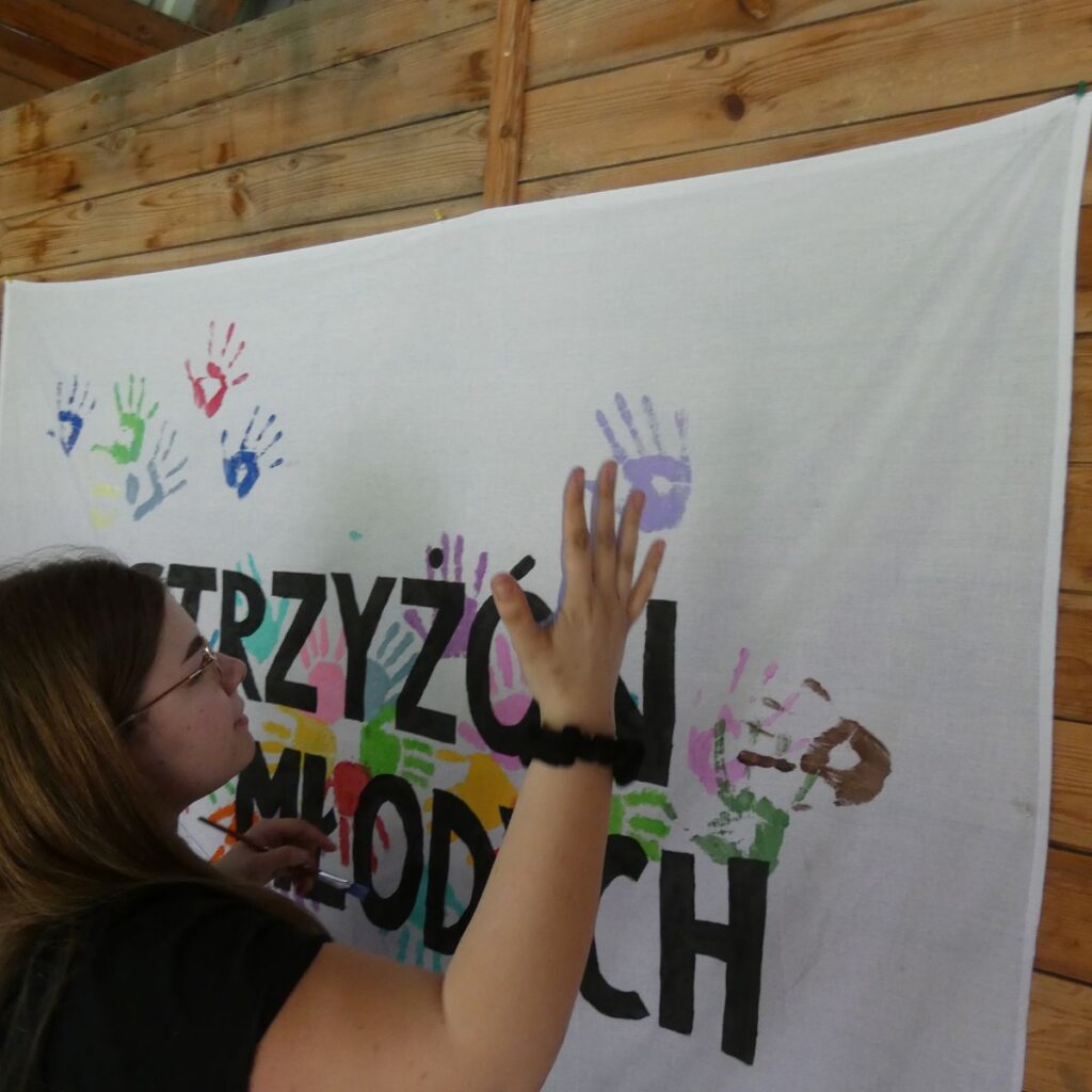 Dziewczyna odbija kolorową dłoń na banerze projektu Strzyżów dla młodych