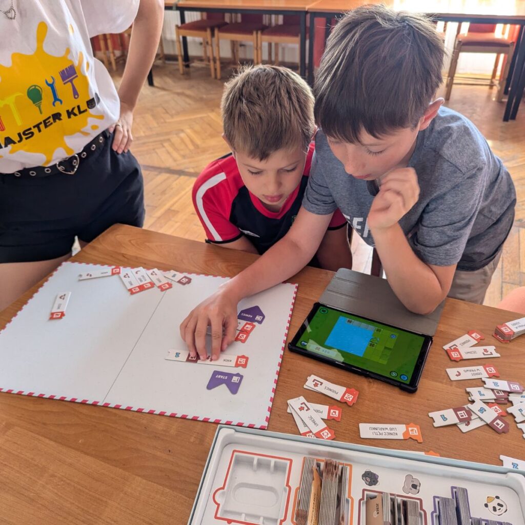 Chłopcy układają elementy programu na planszy podczas zajęć z grą Scottie Go