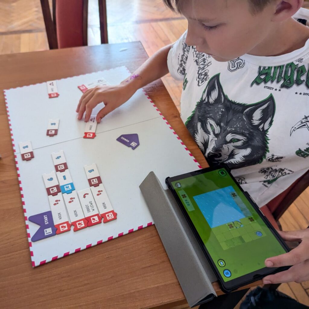 Dziecko układa klocki kodu obok tabletu w trakcie nauki programowania